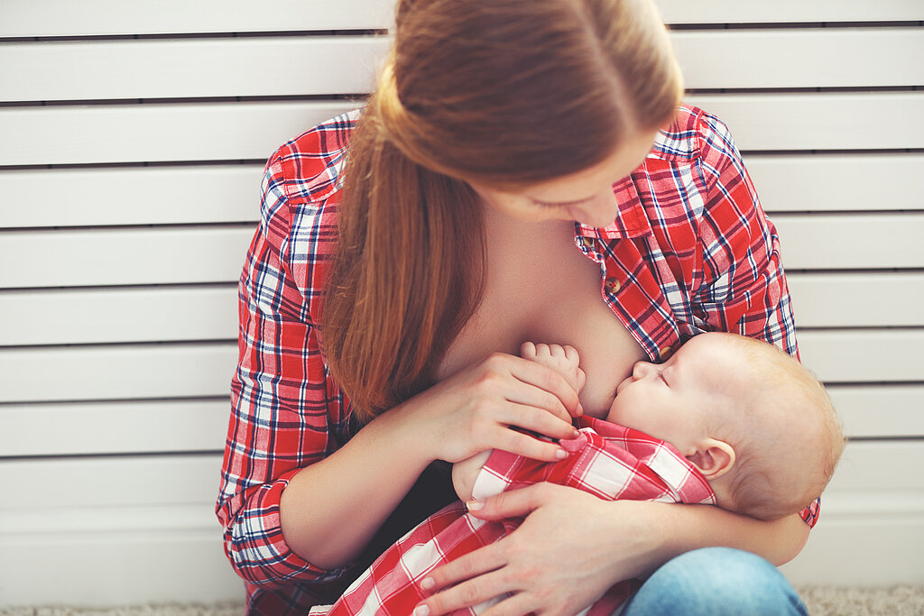 Eine Frau sitzt in der Hocke vor einer Wand und stillt ihr Baby.