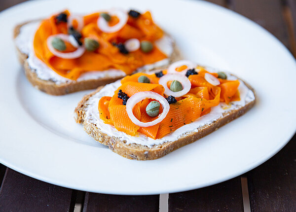 Veganer Karotten-Lox auf zwei Broten mit Frischkäse, Kapern und Zwiebeln, angerichtet auf einem Teller