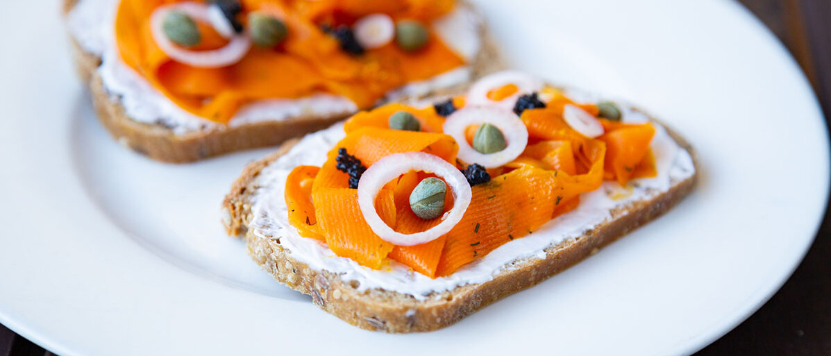 Veganer Karotten-Lox auf zwei Broten mit Frischkäse, Kapern und Zwiebeln, angerichtet auf einem Teller