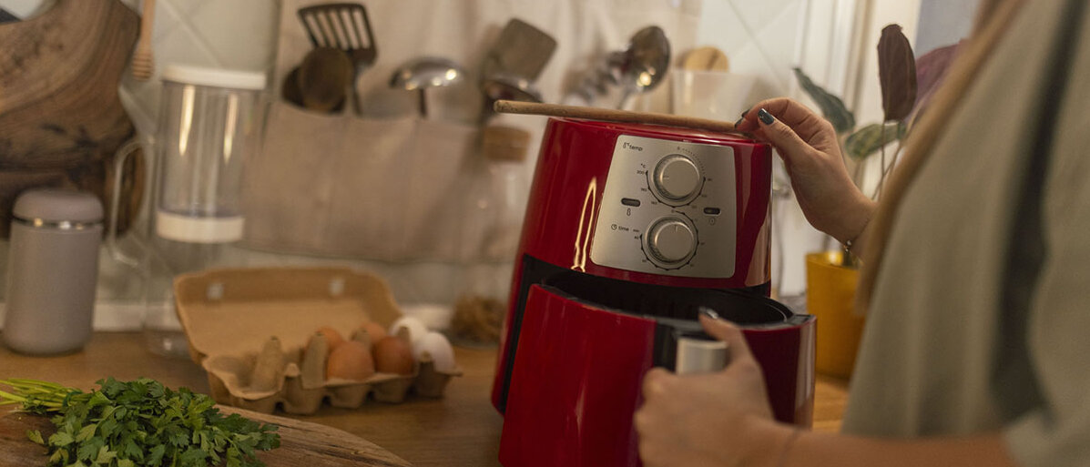 Frau bedient einen roten Airfryer in der Küche