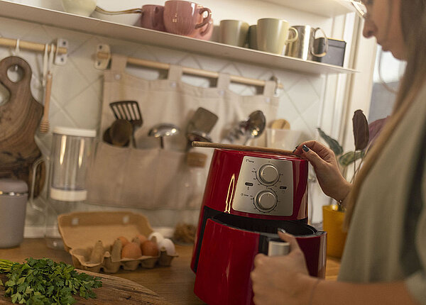 Frau bedient einen roten Airfryer in der Küche