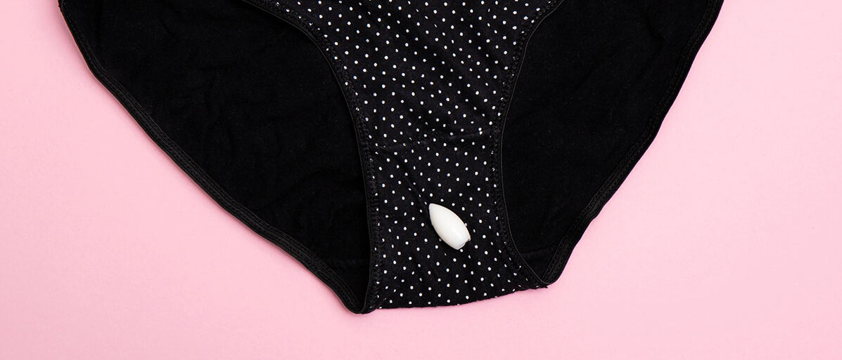 Ein gepunkteter Damenslip liegt auf einer rosa Fläche. Auf dem Zwickel außen liegt ein Vaginalzäpfchen.