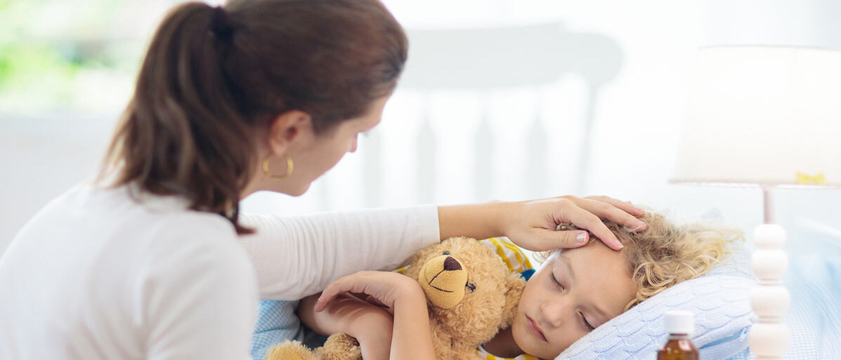 Kranker Junge liegt im Bett und die Mutter hat ihre Hand auf seine Stirn gelegt