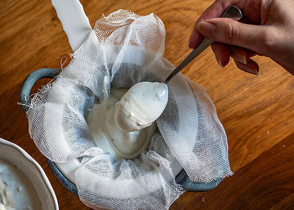 Skyr selber machen Frau die Skyr selbst macht und durch ein Tuch/Sieb gibt