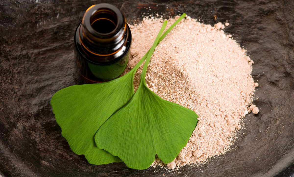 Zwei Ginkgo-Blätter liegen auf einem braunen Pulver, das aus einem Weithalsglas geschüttet wurde.