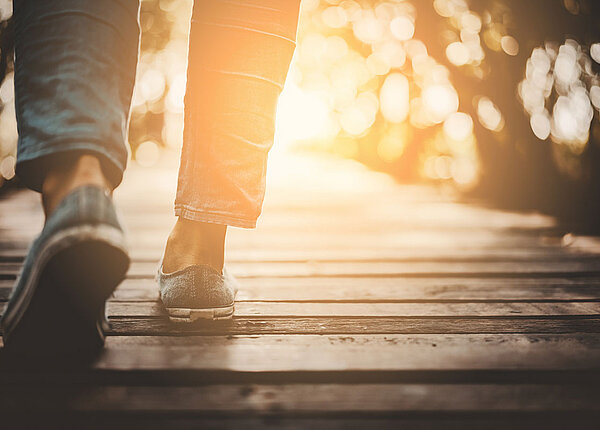 Nahaufnahme: Füße eines Mannes, wie er über bei Sonnenuntergang über einen Steg aus Holz spaziert. 