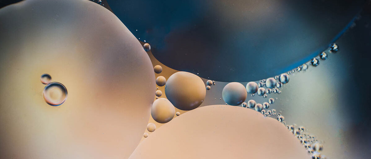 Emulsionen herstellen in der Rezeptur: Alles über Emulgatoren & Co. Zwei Flüssigkeiten, die sich nicht mischen, bilden große und kleine Tröpfchen aufeinander.