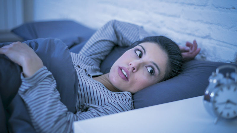 Eine Frau liegt im Dunklen im Bett und starrt auf den Wecker.