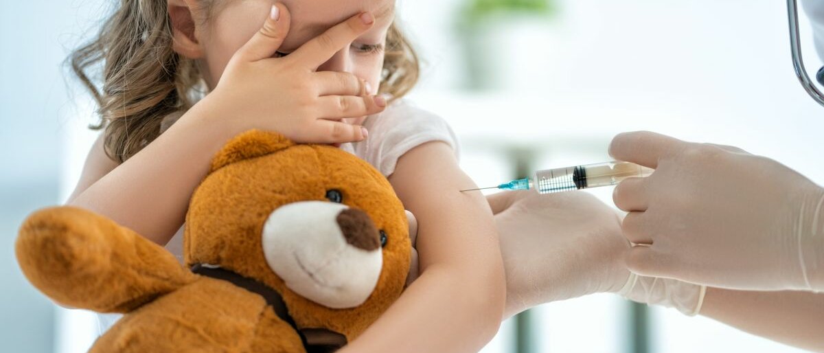 Ein Kind wird geimpft und verdeckt sich halbherzig die Augen.