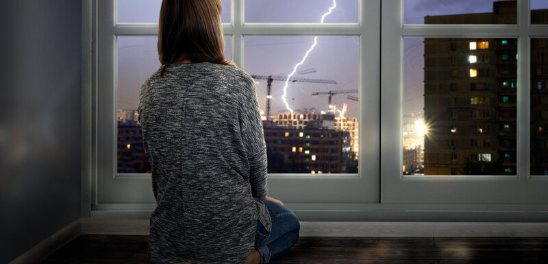 Frau betrachtet Gewitter vor ihrem Fenster