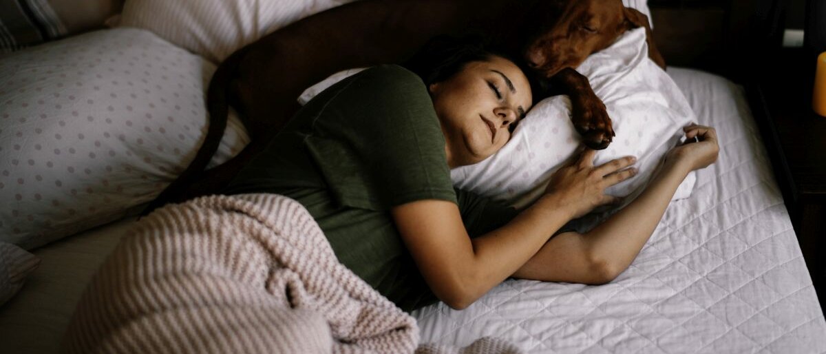 Eine junge Frau liegt mit ihrem Hund im Bett und schläft.