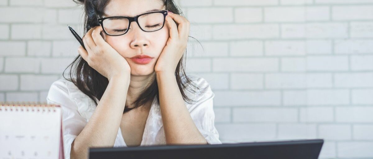 Eine Frau mit Brille sitzt an einem Schreibtisch und schläft fast ein.