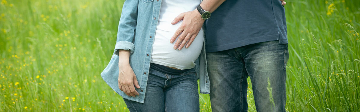 Eine schwangere Frau und ihr Partner auf einer Wiese