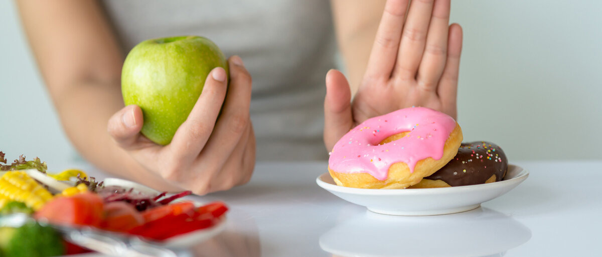 Die linke Hand greift nach einem Apfel, die rechte wehrt Donuts ab.