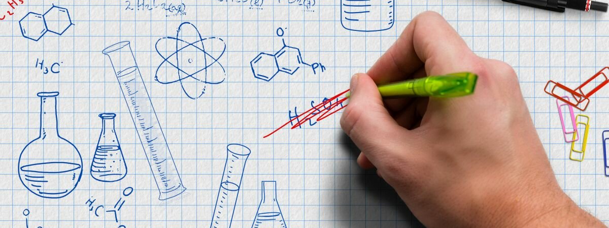 Eine Hand zeichnet chemische Formeln und Bilder auf ein kariertes Blatt Papier.