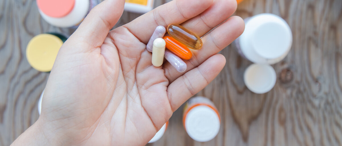 Eine Hand hält viele verschiedene Tabletten und Kapseln in der Hand