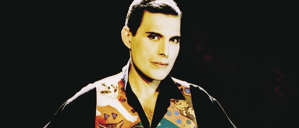 Freddie Mercury Freddie Mercury trÀgt eine bunte Weste mit Katzenmotiven und posiert mit selbstbewusstem Blick.