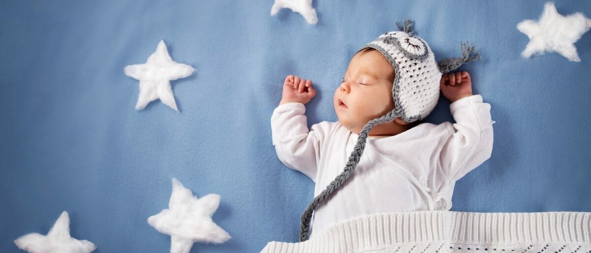 Ein schlafendes Baby mit Mütze auf blauer Decke.