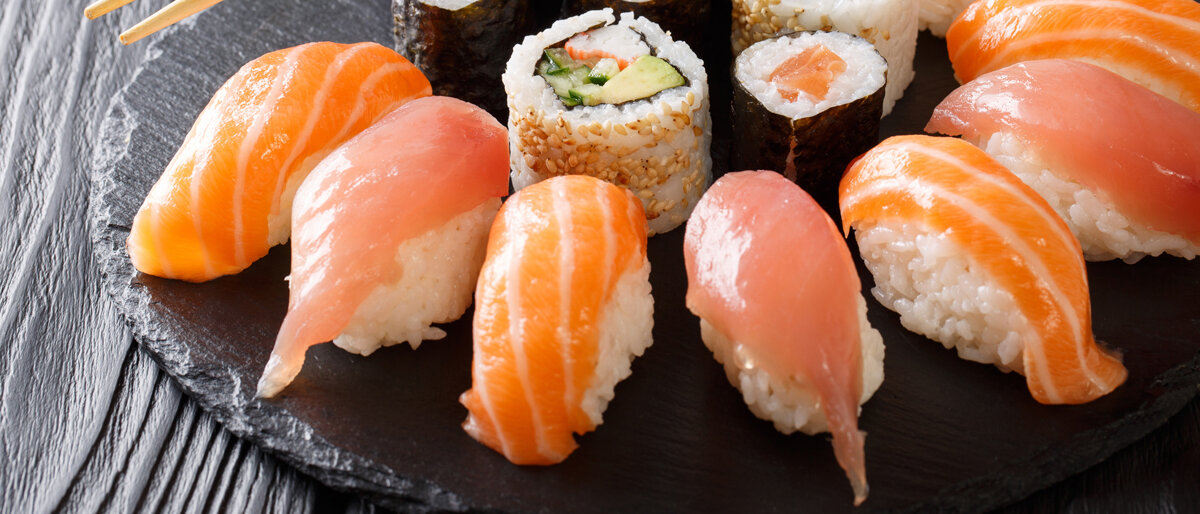 Auf einer Schieferplatte sind verschiedene Nigiri- und Maki-Sushi angeordnet.