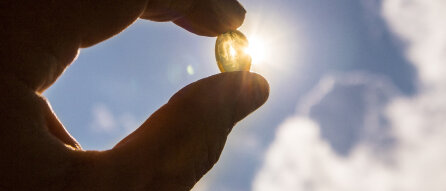 Hand hält Vitamin-D-Kapsel gegen die Sonne