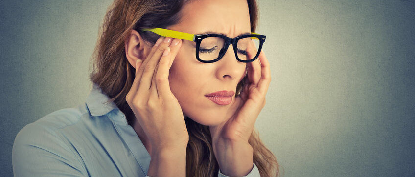 Eine Frau mit Brille reibt sich Stirn und Augen vor Kopfschmerz