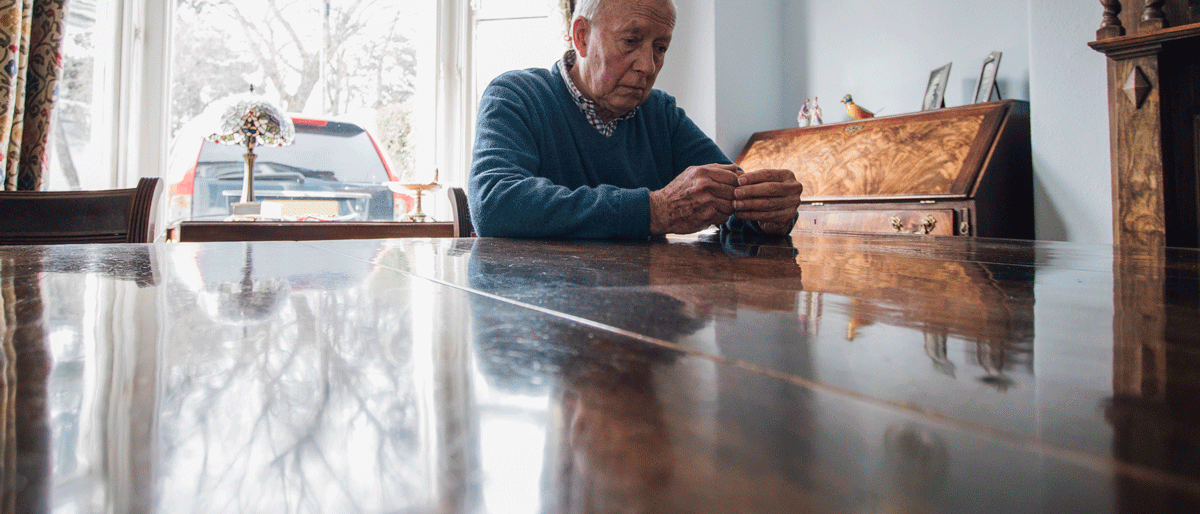 Älterer Mann sitzt traurig und allein an einem großen Holztisch