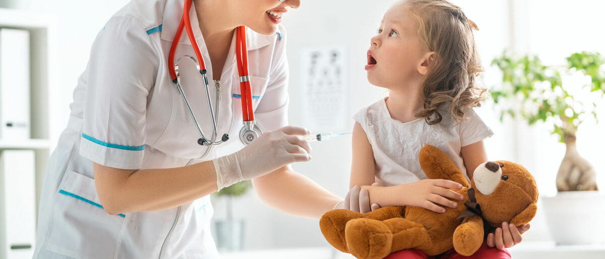 Ein Kind hält Teddy im Arm und wartet auf Impfung durch Kinderärztin