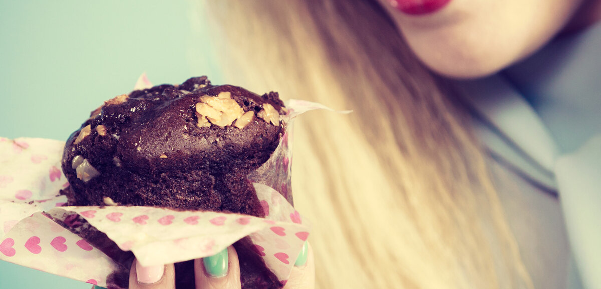 Eine Frau will herzhaft in einen Schoko-Muffin beißen