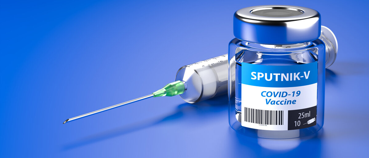 Eine Impfstoffphiole mit der Aufschrift "Sputnik V" liegt mit einer Spritze auf einer blauen Oberfläche.