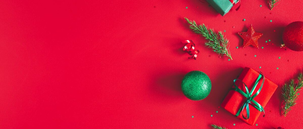Geschenke, Weihnachtskugeln und Tannengrün auf rotem Untergrund.