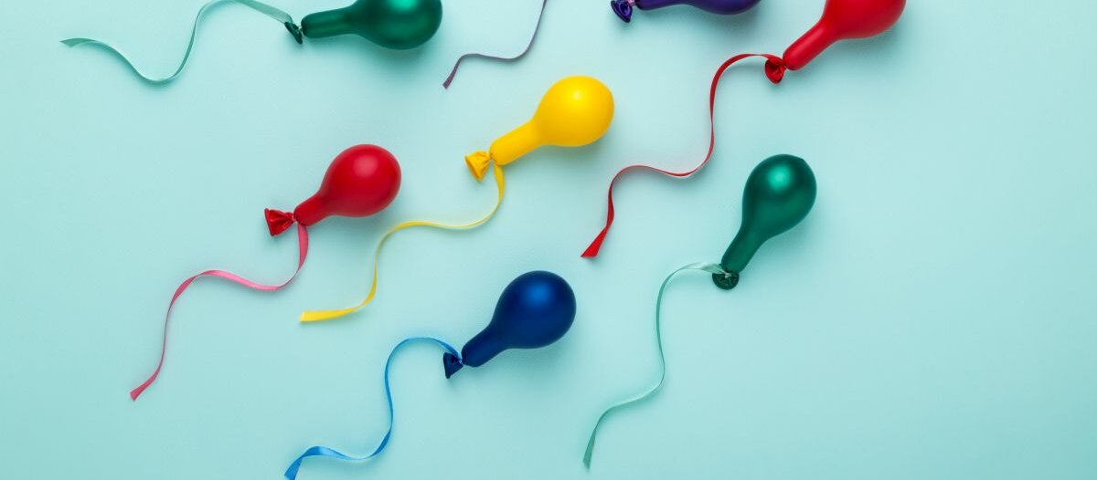 Nur wenig aufgeblasene Luftbalons an Schnüren, die aussehen als seien sie Spermien, auf blauem Untergrund.