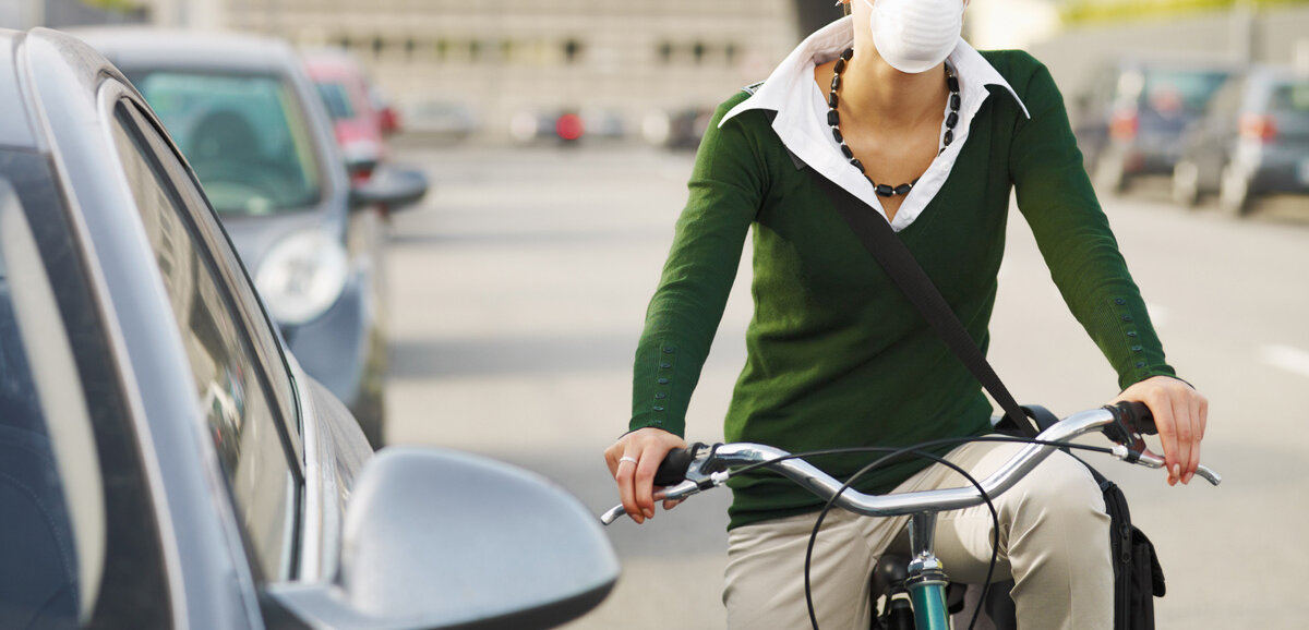 Ein junge Frau fährt mit Atemschutzmaske auf der Straße Fahrrad