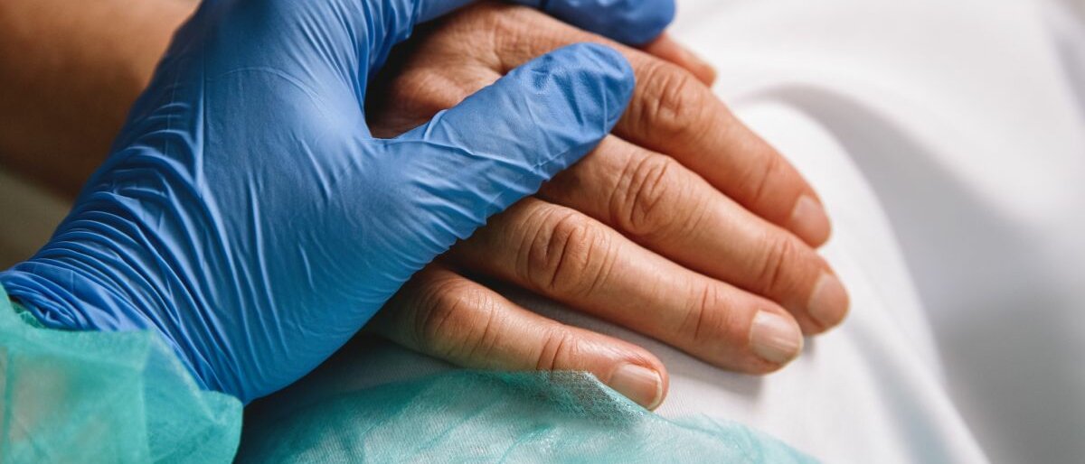 Zwei Hände liegen übereinander: Eine Hand gehört zu einer alten Frau, die andere einem Arzt.