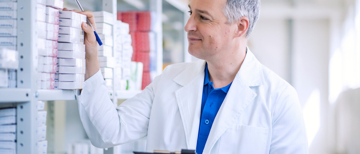 ein lächelnder Mann im weißen Kittel kontrolliert Arzneimittellagerbestände