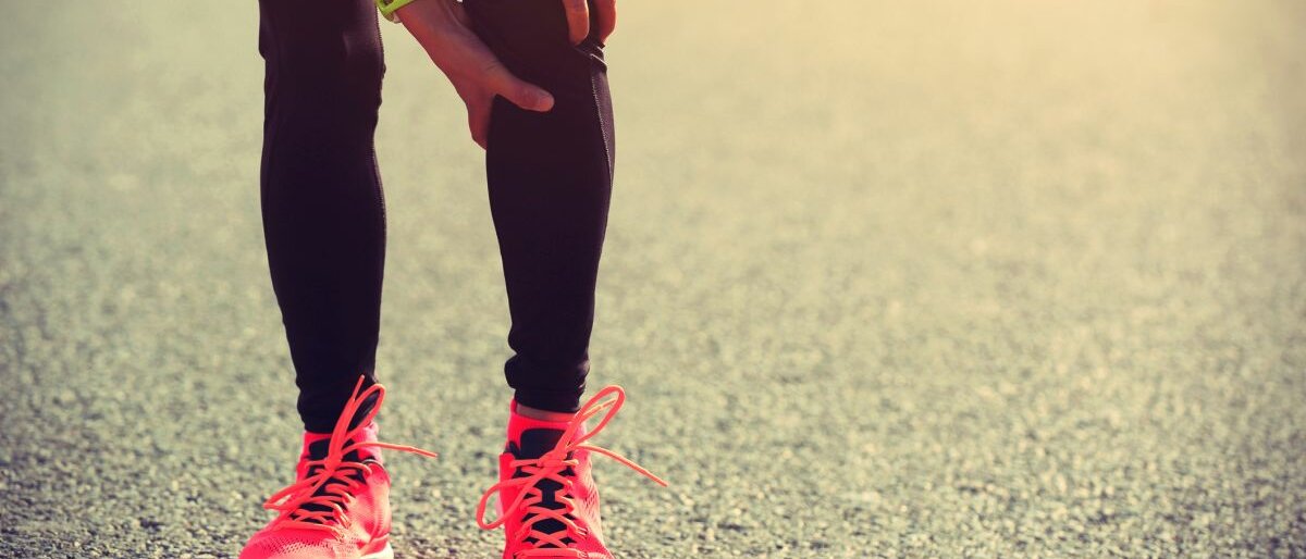 Eine Joggerin steht auf einer Straße und greift sich ans Knie.