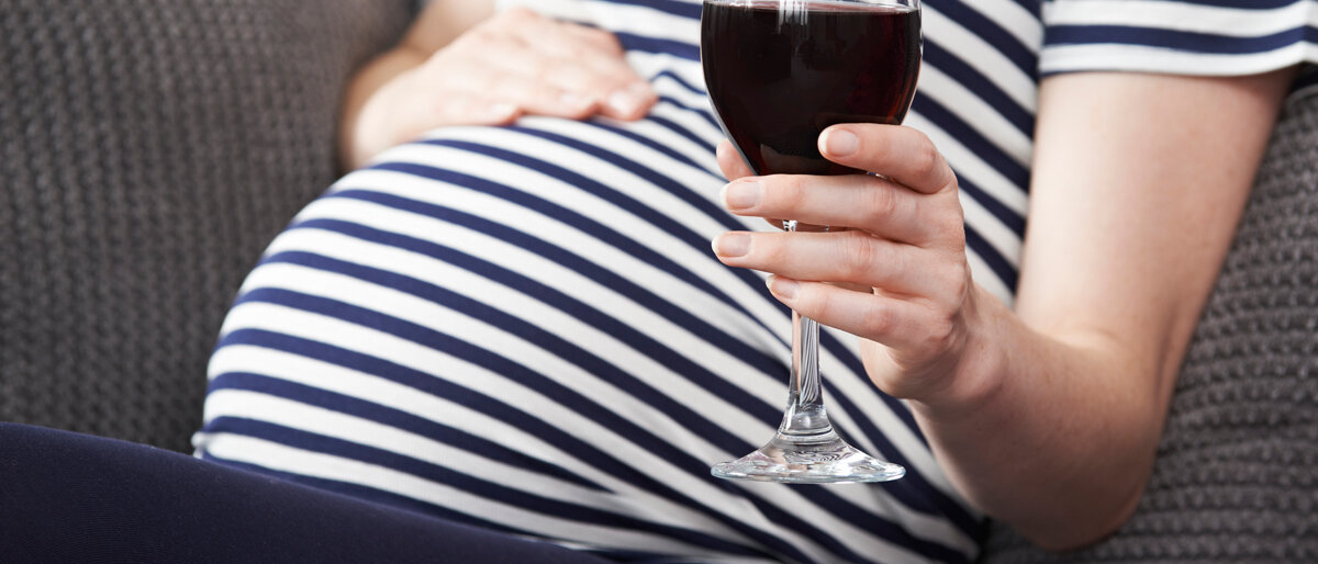 Schwangere Frau trinkt ein Glas Rotwein