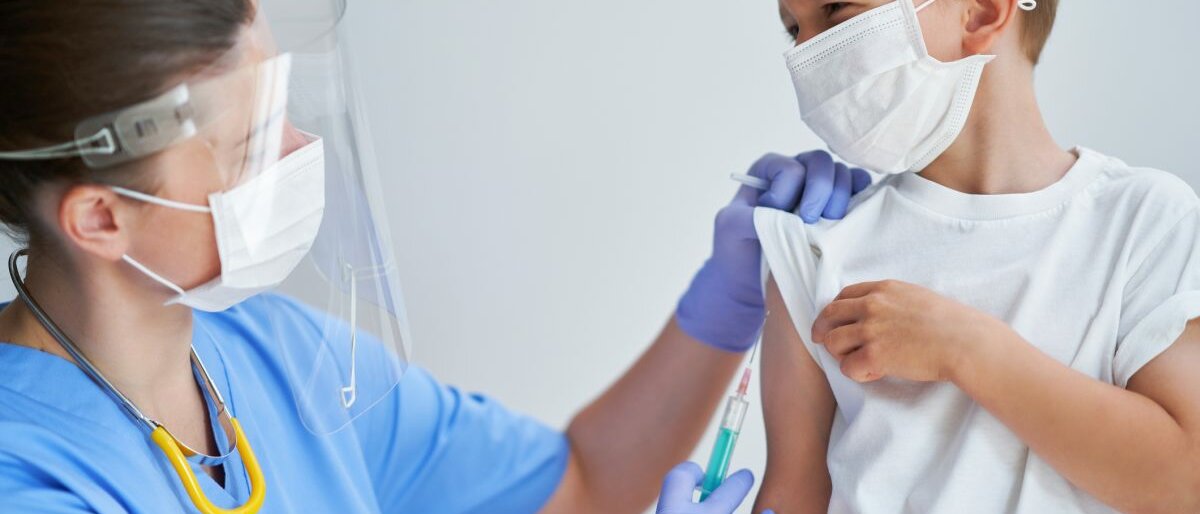 Ein Kind mit Atemschutzmaske wird geimpft.